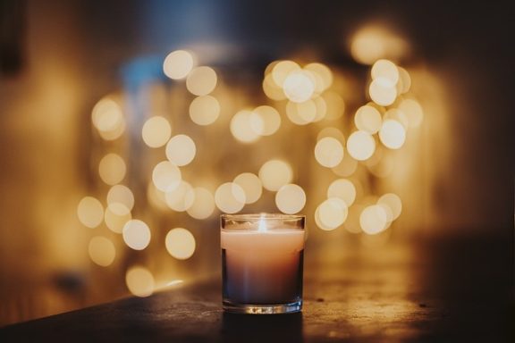Kerze auf einem Tisch, im Hintergrund unscharfe, leuchtende Lichter.