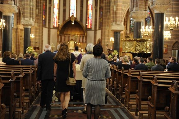 Beerdigung in einer Kirche mit Zuschauern und nahen Anwesenden im Hintergrund.
