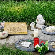 Gedenkstätte mit Steinen, Kerzen und einer Plakette auf einer grünen Wiese.