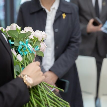Eine Person in schwarzer Jacke hält einen Strauß rosa Rosen mit blauen Bändern.