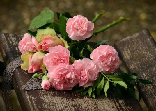 Ein Strauß rosa Rosen mit grünem Laub auf einer Holzoberfläche.