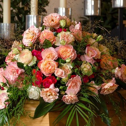 Bunter Blumenschmuck mit Rosen, Nelken und grünem Blattwerk in elegantem Arrangement.