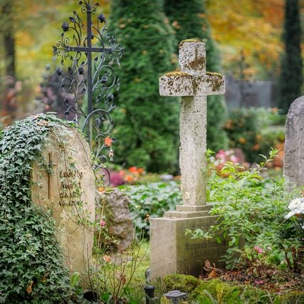 Gräber mit einem Kreuz, umgeben von bunten Blumen und grünen Büschen.